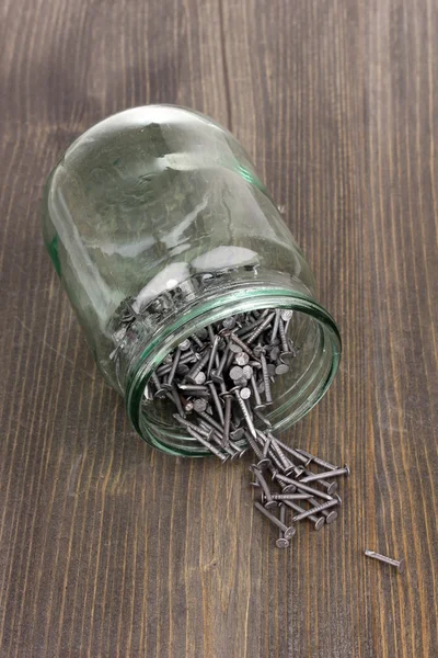 Pregos de metal e frasco de vidro no fundo de madeira — Fotografia de Stock