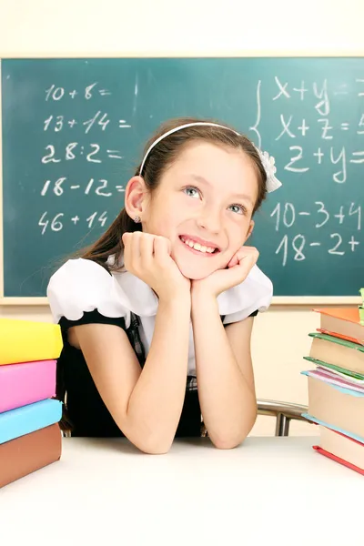 Little schoolgirl and books in classroom near blackboard — Stock Photo, Image