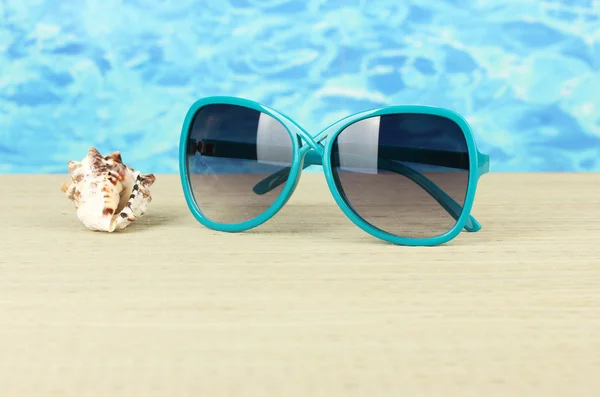 Eleganti occhiali da sole da donna con guscio sul tappeto di paglia su fondo acqua — Foto Stock