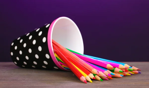 Кольорові олівці в склі на дерев'яному столі на фіолетовому фоні — стокове фото