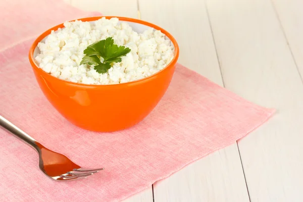 Cottage cheese with parsley in orange bowl and fork on pink napkin on white wooden table close-up — Stock Photo, Image