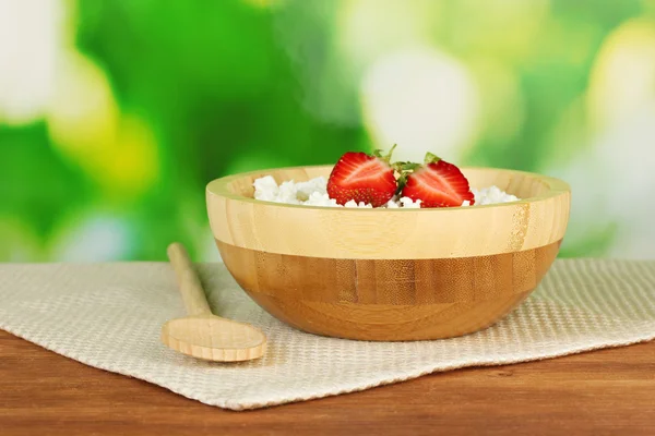 Cottage cheese with strawberry in wooden bowl with wooden spoon on beige napkin on wooden table on green background