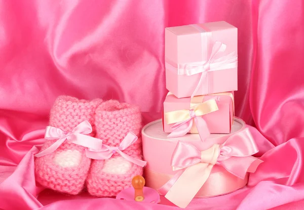 Rosa baby stövlar, napp, gåvor på silk bakgrund — Stockfoto