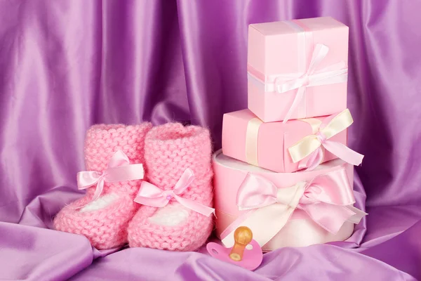 Pink baby laarzen, fopspeen, geschenken op zijde achtergrond — Stockfoto