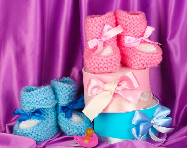 Pink and blue baby boots, pacifier and gifts on silk background — Stock Photo, Image