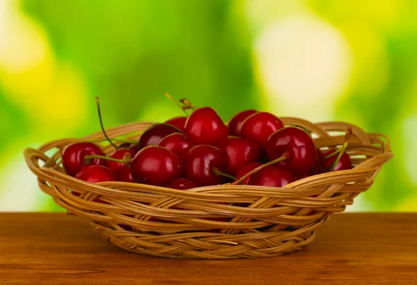 Cherry in wicker bowl on wooden table on green background — Stock Photo, Image