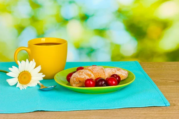 Croissant com cerejas e café em mesa de madeira em fundo verde — Fotografia de Stock