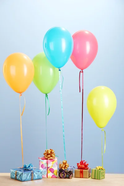 Красочные воздушные шары с подарками на деревянном столе на голубом фоне — стоковое фото