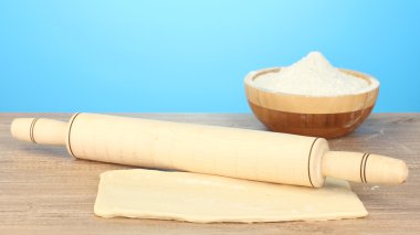 The dough with a rolling pin on wooden table on blue background clipart