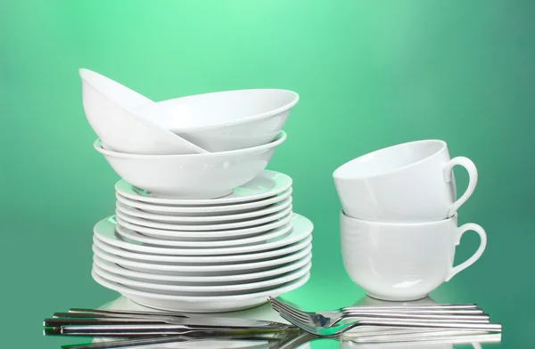 Чистые тарелки, чашки и столовые приборы на зеленом фоне — стоковое фото