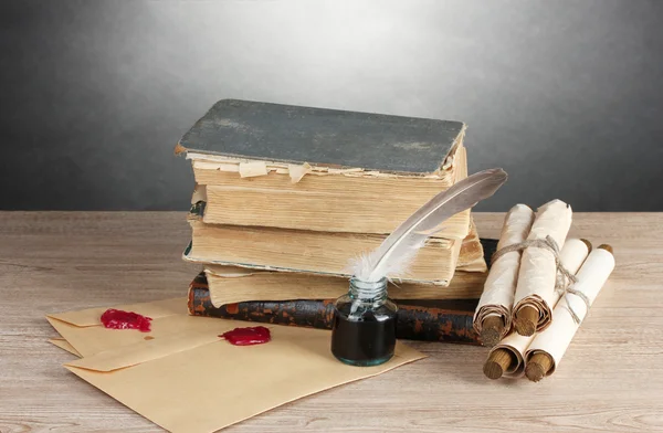 stock image Old books, scrolls, feather pen and inkwell on wooden table on grey background