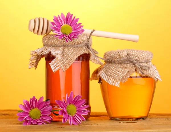 Söt honung i burkar med drizzler på träbord på gul bakgrund — Stockfoto