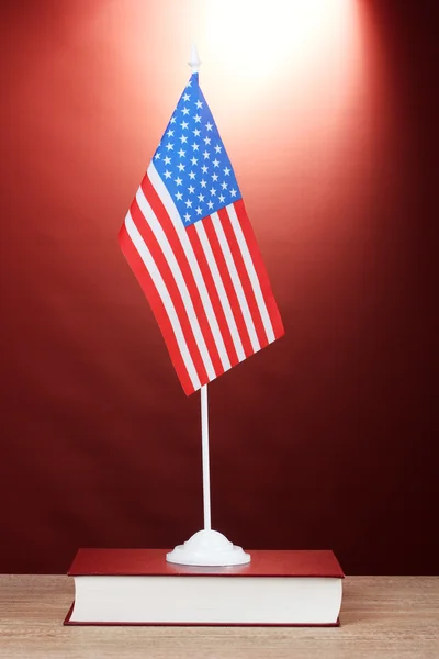 Bandera americana en el stand y libro sobre mesa de madera sobre fondo rojo —  Fotos de Stock