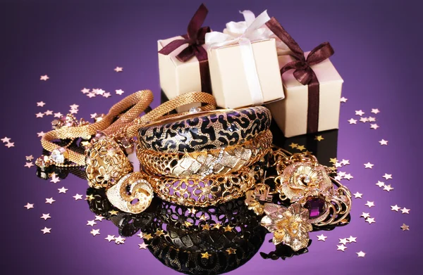 Schönen goldenen Schmuck und Geschenke auf lila Hintergrund — Stockfoto