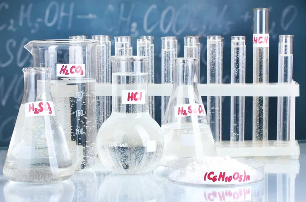 Пробирки с различными кислотами и другими химикатами на фоне доски — стоковое фото