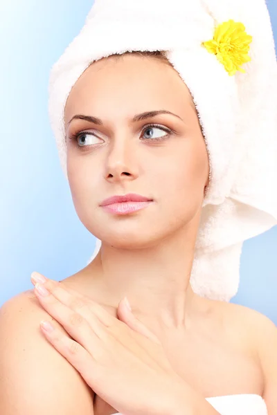 Vacker ung kvinna som efter dusch med en handduk och ljust gul blomma på huvudet på blå bakgrund närbild — Stockfoto