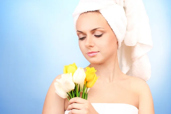 Beautiful young woman after shower with a towel on her head and with a bouquet of tulips on blue background close-up — Stock Photo, Image