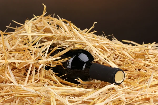 Láhev značkového vína na seno na hnědé pozadí — Stock fotografie