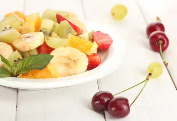 Insalata di frutta fresca su piatto e bacche su tavolo di legno bianco — Foto Stock