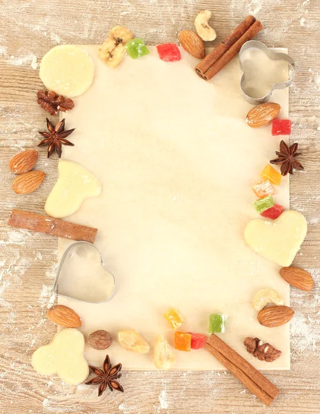 Marco hecho de fruta confitada, frutos secos, galletas sin cocer y moldes para galletas en primer plano pergamino —  Fotos de Stock