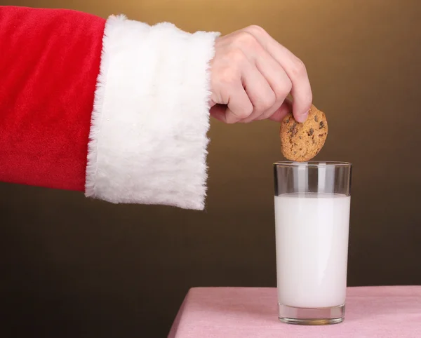 Рука Санта Клауса держит шоколадное печенье на коричневом фоне — стоковое фото