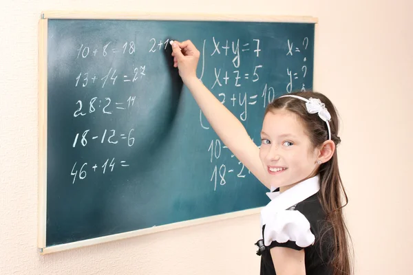 Schönes kleines Mädchen schreibt auf Klassenzimmertafel Stockbild