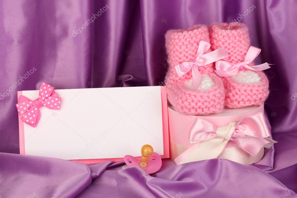 Pink baby boots, pacifierd, postcard and gifts on silk background