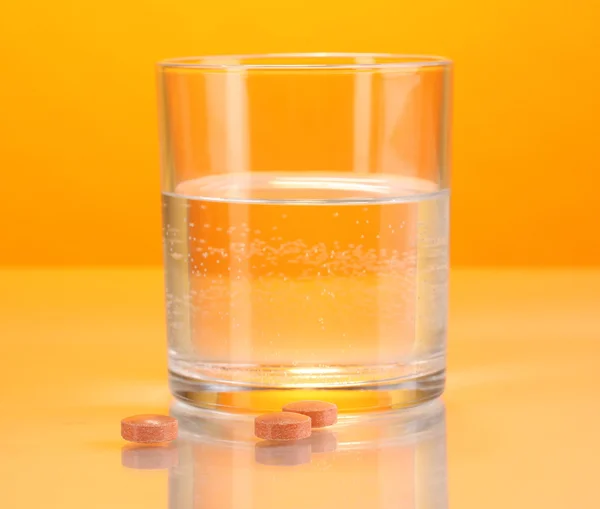 Glass of water and pills on orange background — Stock Photo, Image
