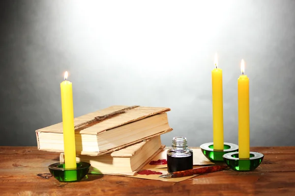 Libri antichi, pergamene, calamaio penna inchiostro e candele su tavolo in legno su sfondo grigio — Foto Stock