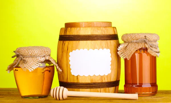Miel dulce en frascos y barril con rociador sobre mesa de madera sobre fondo verde — Foto de Stock