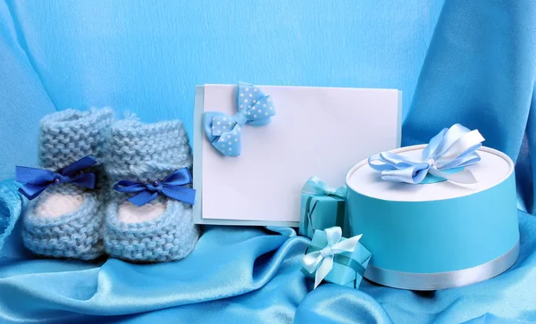 Schöne Geschenke, Babystiefel, leere Postkarte und Schnuller auf blauer Seide — Stockfoto