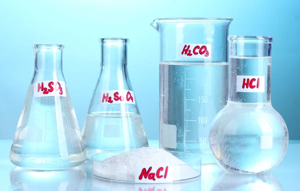 Tubos de ensaio com vários ácidos e produtos químicos sobre fundo azul — Fotografia de Stock