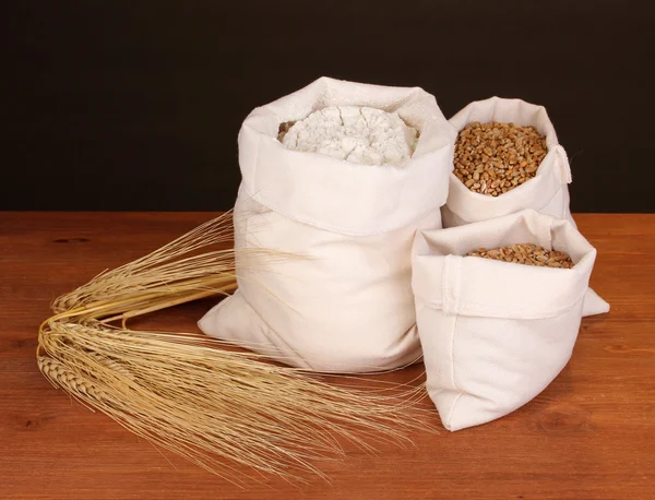Mehl und Weizenkorn auf Holztisch vor dunklem Hintergrund — Stockfoto