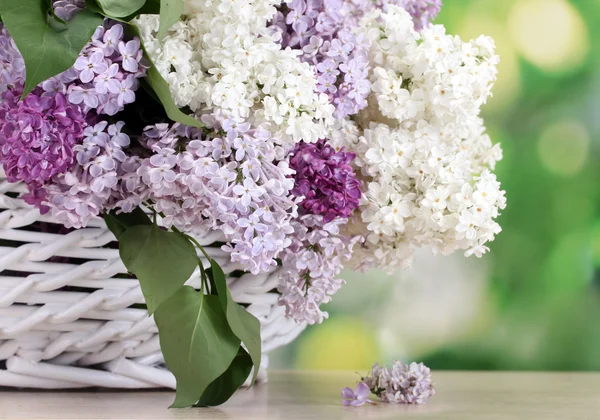 Красивые сиреневые цветы в корзине на деревянном столе на зеленом фоне — стоковое фото