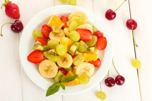 Vers fruit salade op plaat en bessen op witte houten tafel — Stockfoto