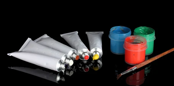 Tubes with colorful watercolors and jars with gouache and brush on black background close-up — Stok fotoğraf