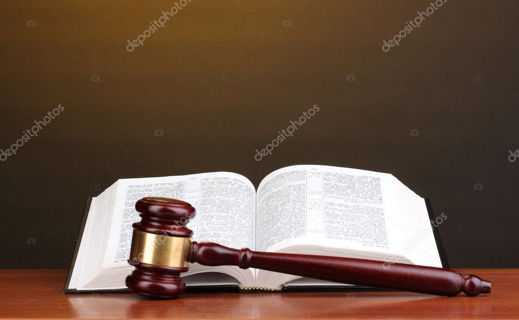 Judge's gavel and open book on wooden table on brown background