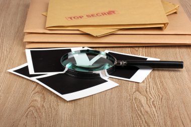 Envelopes with top secret stamp with photo papers and magnifying glass on wooden background clipart