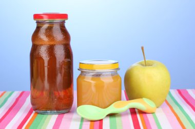 Jar of baby puree and juice with spoon on napkin on blue background