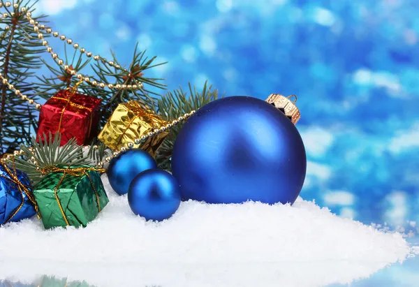 Weihnachtskugel und Spielzeug mit grünem Baum im Schnee auf blau — Stockfoto