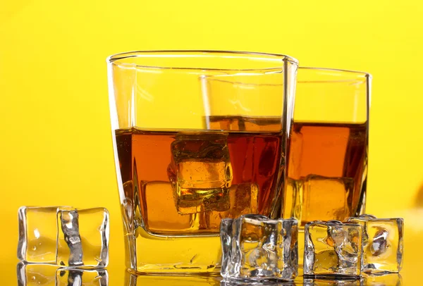 两个眼镜的苏格兰威士忌和黄色背景上的冰 — 图库照片