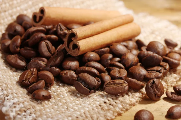 Kaffebönor och kanelstänger på säckväv på träbord — Stockfoto