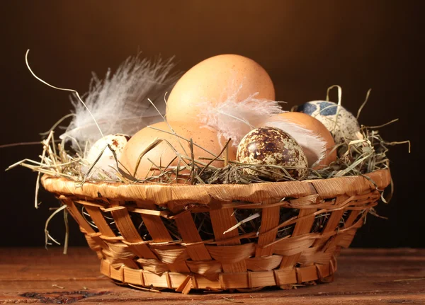Hühner- und Wachteleier in einem Nest auf Holztisch auf braunem Hintergrund — Stockfoto