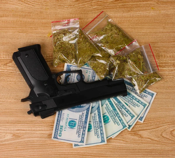 Marihuana v obalech, dolary a pistole na dřevěné pozadí — Stock fotografie