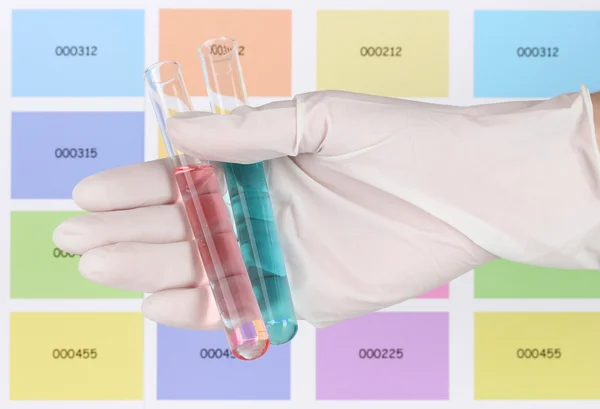 Two tubes with red and blue liquid in hand on color samples background — Stock Photo, Image