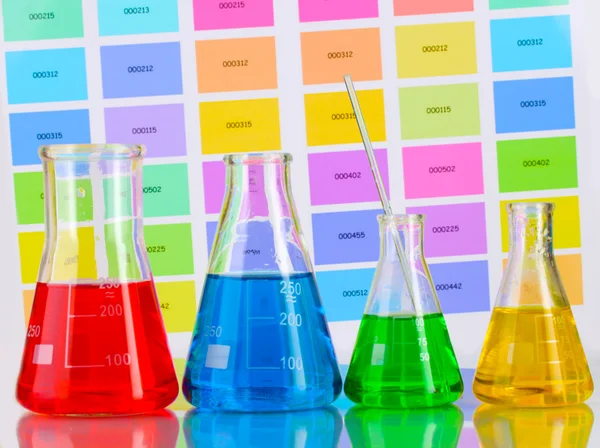 Laboratory flasks with color liquid on color samples background — Stock Photo, Image