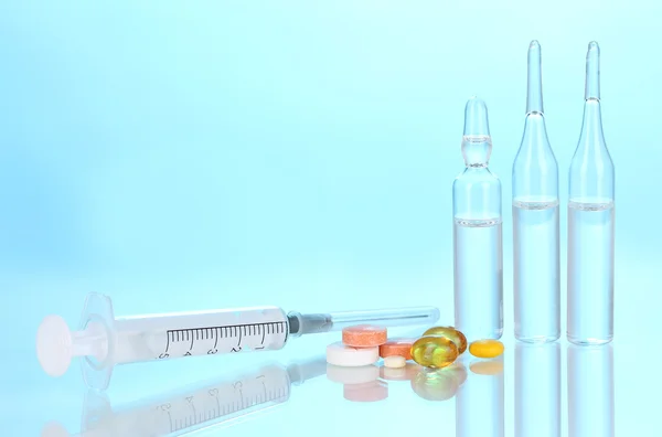 Jeringa con ampollas y tabletas médicas sobre fondo azul —  Fotos de Stock