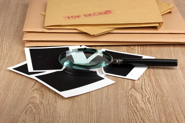 Конверты со сверхсекретной печатью с фотобумагой и увеличительным стеклом на деревянном фоне — стоковое фото