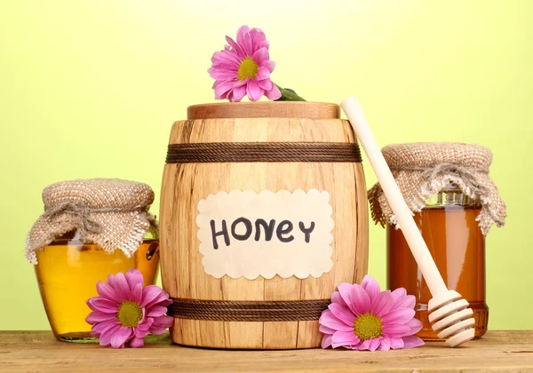 Miel dulce en barril y frascos con rociador sobre mesa de madera sobre fondo verde — Foto de Stock