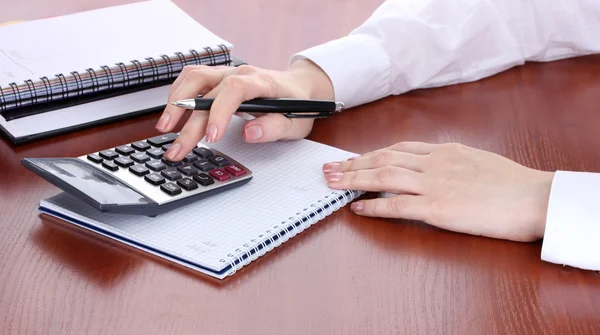 Женские руки с карандашом, блокнотами и калькулятором на деревянном столе — стоковое фото